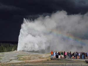 Old Faithful Geyser erupts with dark skies behind and a rainbow before, Upper Geyser Basin, Yellowstone National Park, Wyoming