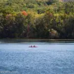 A canoe paddles on Canadice Lake below fall colors, New York
