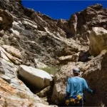 A hiker approaches a rocky wall in a desert canyon