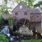 A brown building with a water wheel with a waterfall on the left