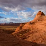 Majestic clouds over red rocks and distant views with a trail marked on the rock with stones