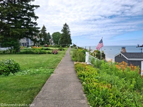 A sidewalk travels between a lawn and a garden with views out to a lake
