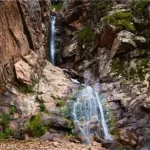 A waterfall tumbles in two stages down a cliff face