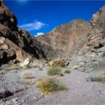 A desert canyon filled with gravel and brush bounded by rocky cliff walls