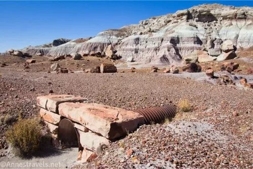 A culvert in a stone wall under a dirt roadbed with petrified wood and badlands in the background