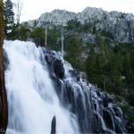 A waterfall tumbles down rocks with cliffy mountains in the background