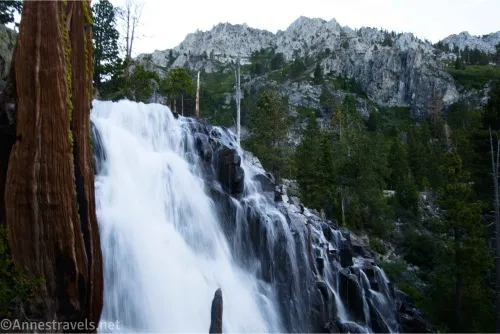 A waterfall tumbles down rocks with cliffy mountains in the background