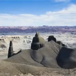 Fantastic dark formations in front of lighter desert with distant mountains under clouds in a blue sky