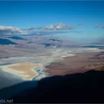 Views into a desert valley with a lake with clouds above and blue skies