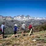 Four hikers walk through grassy Deadman Pass with the Minaret mountain peaks behind them
