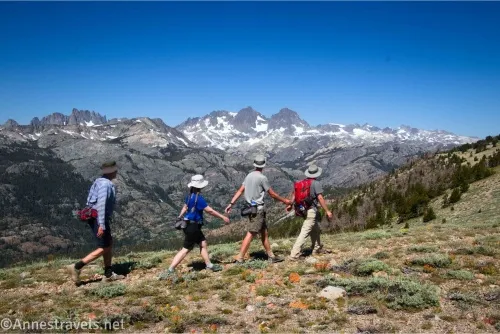 Four hikers walk through grassy Deadman Pass with the Minaret mountain peaks behind them