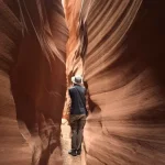 A hiker stands in a very narrow, sculpted slot canyon