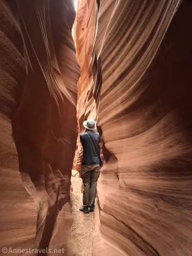 A hiker stands in a very narrow, sculpted slot canyon