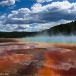 Colorful drainage channels and spring at the Grand Prismatic Spring below puffy white clouds in Yellowstone National Park