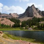 A blue Blanch Lake below craggy mountains with a hiker on a trail beside the lake