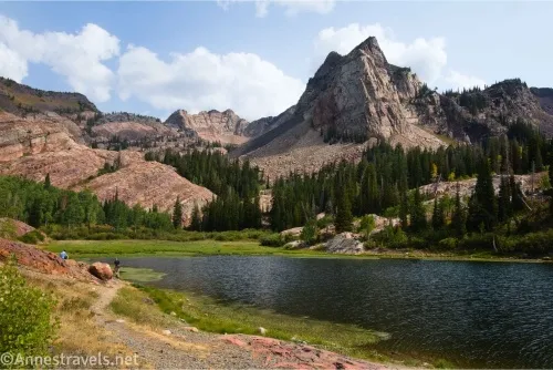 A blue Blanch Lake below craggy mountains with a hiker on a trail beside the lake
