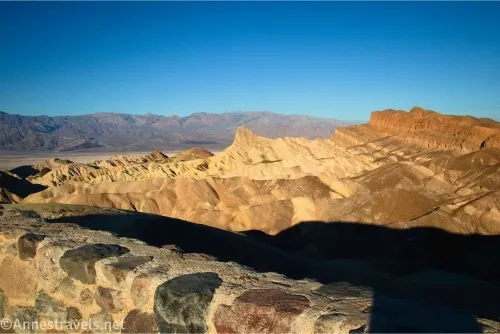 A stone wall around Zabriskie Point with views to yellow badlands around Manly Beacon and the red cliffs of the Red Cathedral Canyon Crest in Death Valley National Park